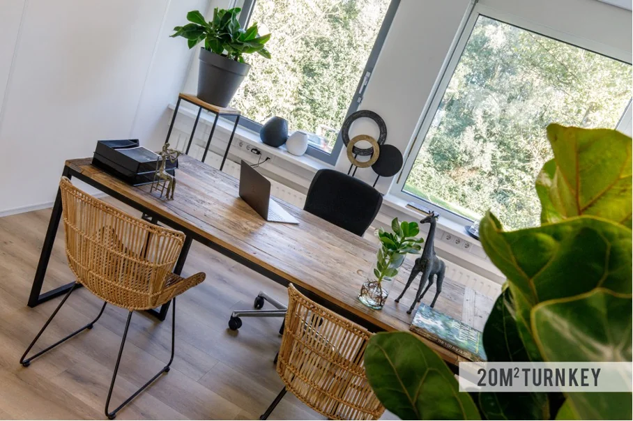 Modern ingerichte kantoorruimte aan de Baarnsche Dijk met houten bureau, rotan stoelen, planten en grote ramen met uitzicht op groen.